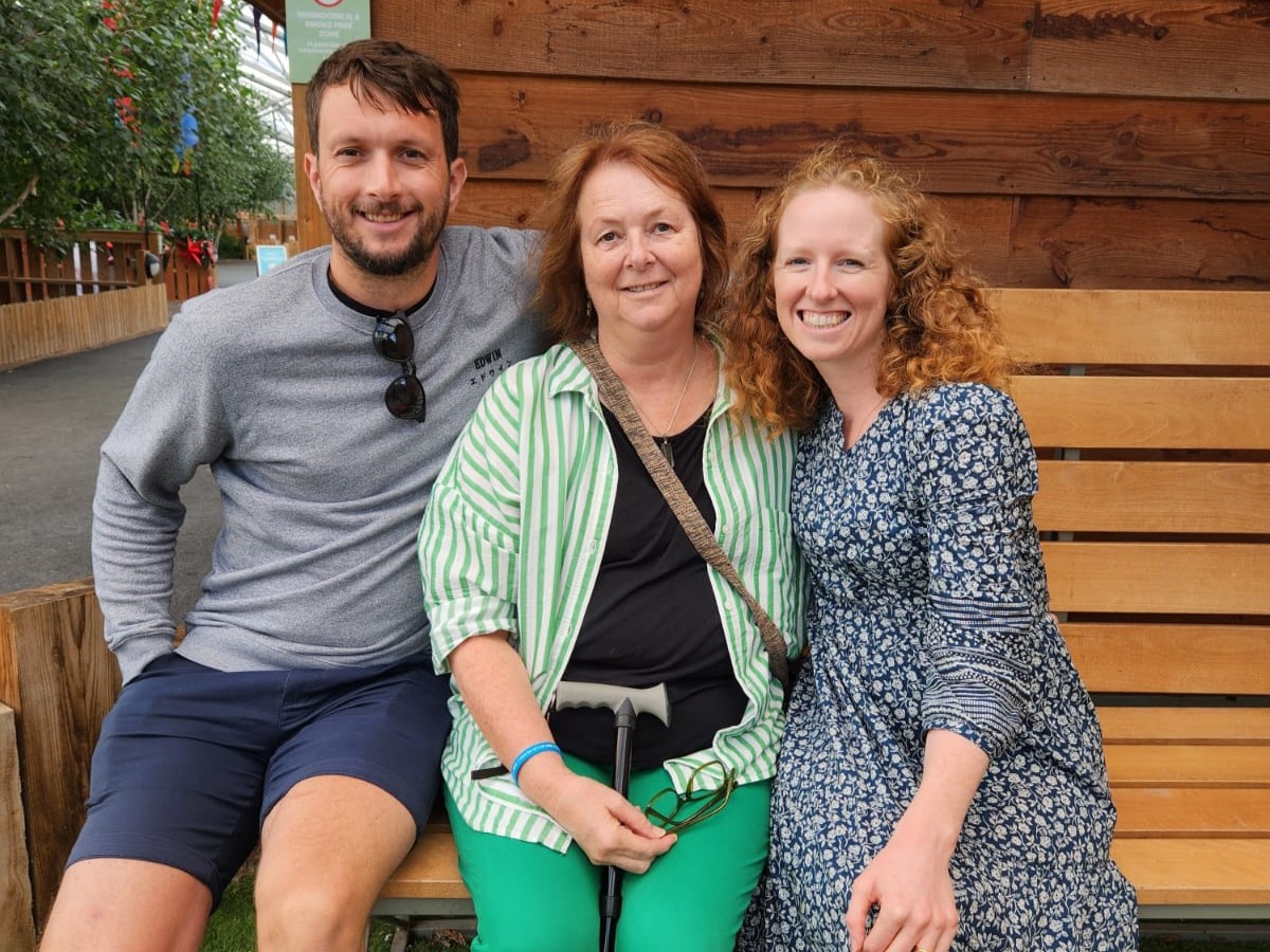 3 people sitting on a bench, smiling at the camera. Diana is in the middle, with her son on the left and her daughter on the right.